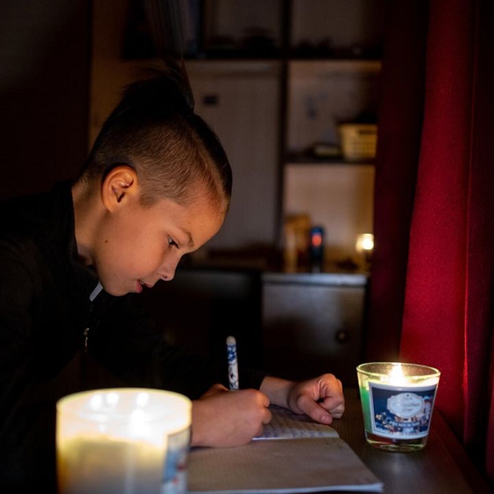 Ukraine: Ein Junge sitzt in einem dunklen Raum bei Kerzenlicht und macht seine Hausaufgaben.