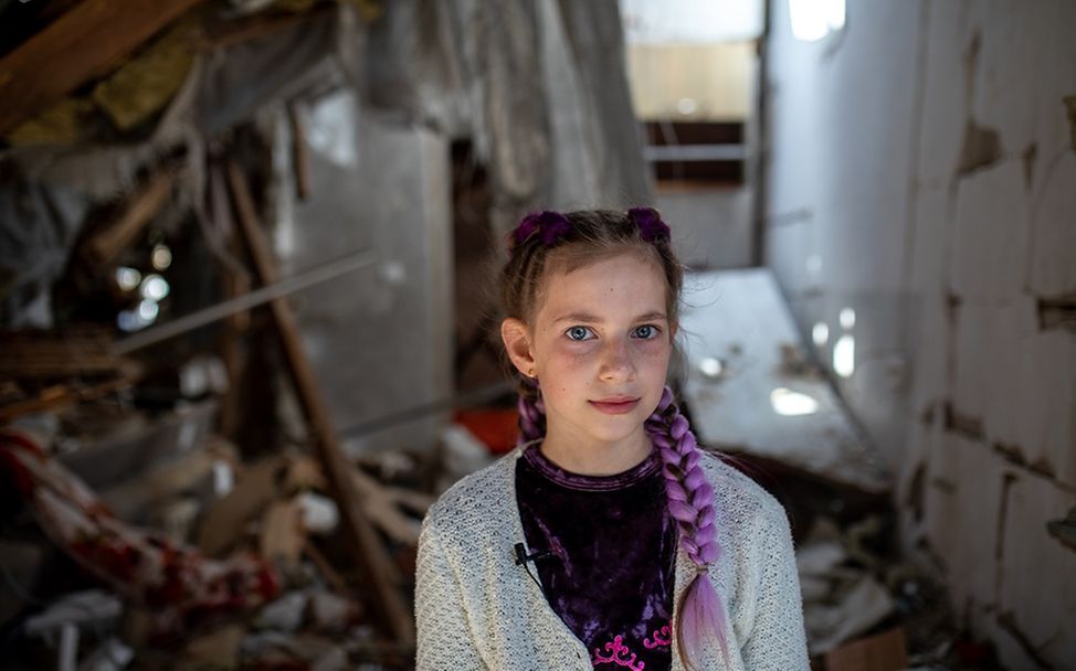 Ukraine: Ein Mädchen steht vor einem zerstörten Haus.