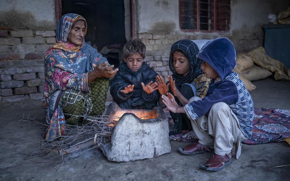 Frau mit Enkelkindern zum Warmhalten an einer Feuerstelle in Dadu