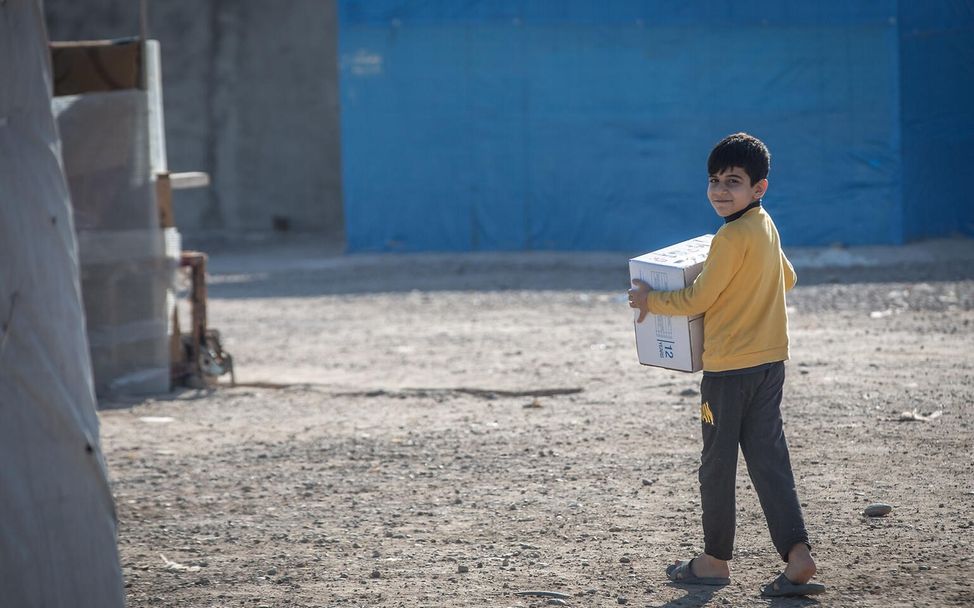 Mohammed aus dem Flüchtlingslager Baharka in Erbil, hält ein Paket mit Winterkleidung von UNICEF in der Hand.