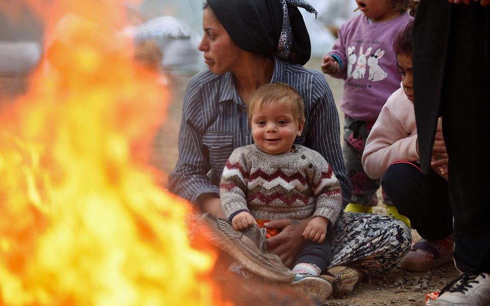 Spenden Türkei: Eine Mutter sitzt mit ihrem Baby kurz nach dem Erdbeben an einem wärmenden Feuer in einer Notunterkunft.