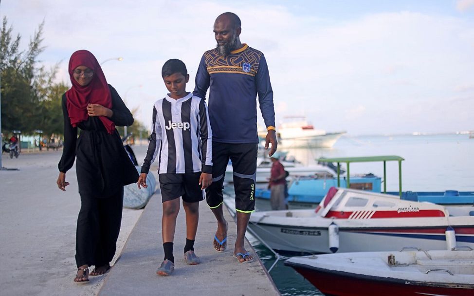 Malediven: Fathimath spaziert mit ihrem Vater und ihrem Bruder am Hafen entlang, neben ein paar kleinen Booten.