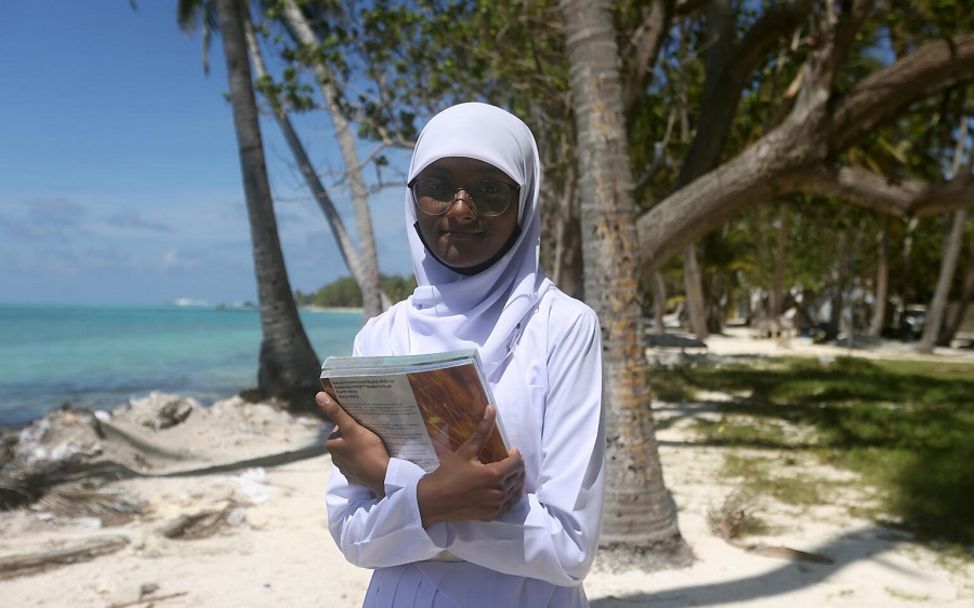 Malediven: Fathimat steht mit ihren Schulbüchern in der Hand am Strand.