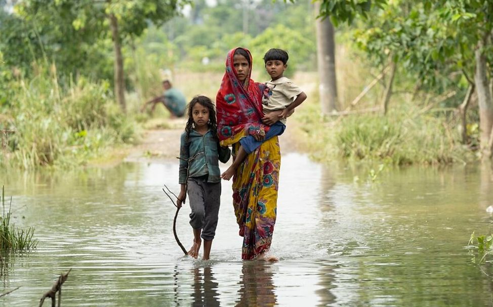 Bangladesch: Drei Kinder laufen über einen überschwemmten Weg.