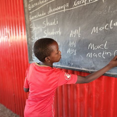 Adan schreibt an die Tafel des Lernzentrums im Binnenvertriebenenlager in Deebwin, Somalia.