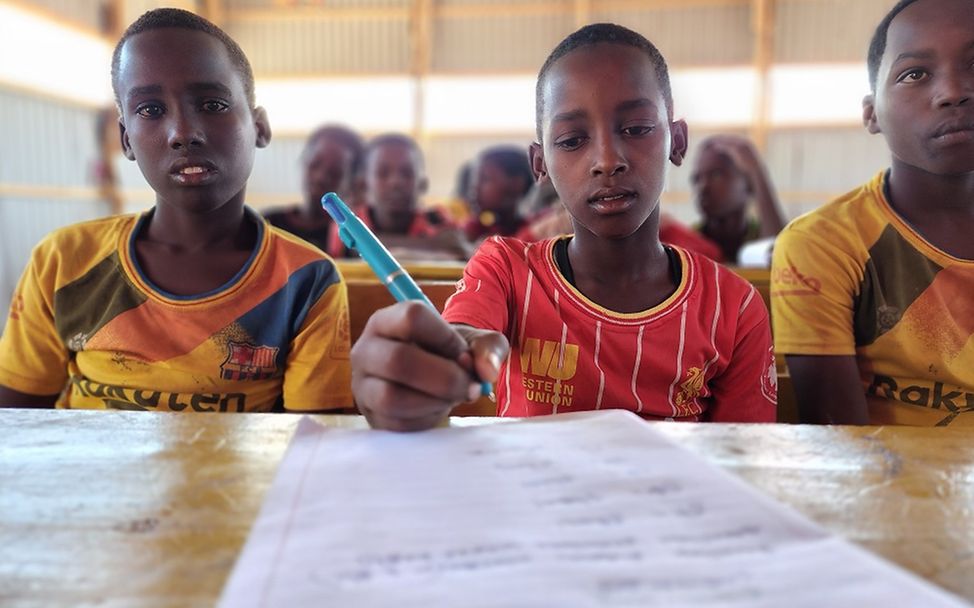 Somali: Adan sitzt neben seinen Klassenkameraden an einem Tisch und schreibt. 