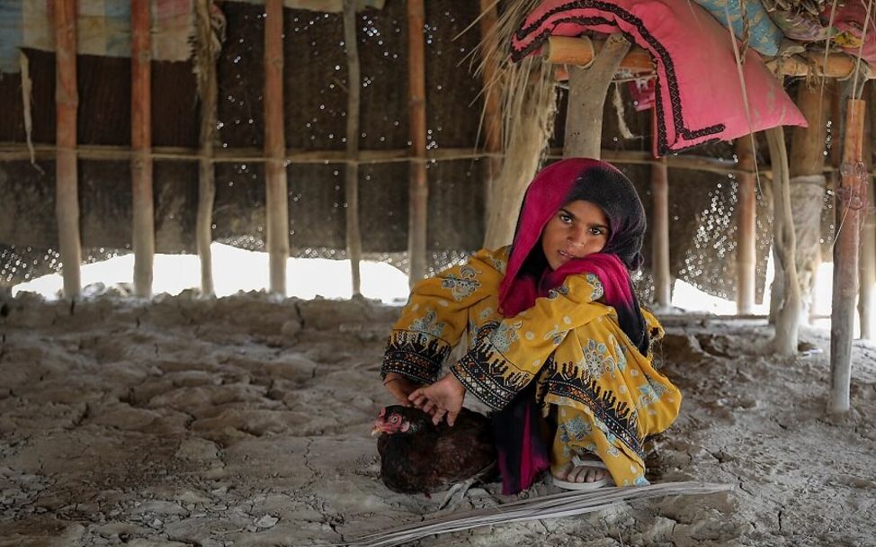 Pakistan: Rukhsana sitzt auf dem Boden mit einem dunkel-braunen Huhn im Schoß.