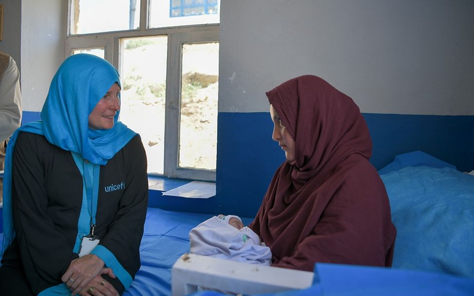 Afghanistan: Eine UNICEF-Mitarbeiterin sitzt mit einer Mutter und ihrem Neugeborenen auf einem Bett.
