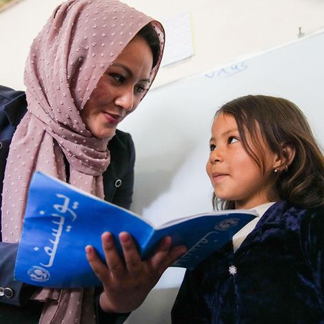 Afghanistan: Eine Lehrerin schaut mit einem Mädchen in ihr Hausaufgabenheft 