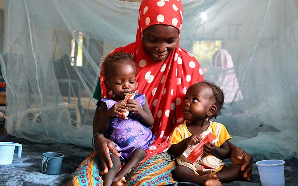 Niger Mangelernährung: Eine Mutter hält ihre Erdnusspaste essenden Zwillinge auf dem Schoß. 