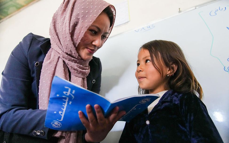 Afghanistan Bildung für Mädchen: Eine Lehrerin schaut mit einem Mädchen in ihr Hausaufgabenheft 