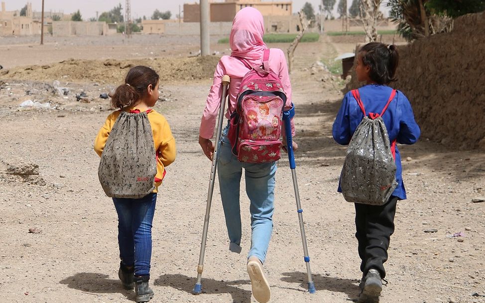 Syrien: Ein Mädchen auf Krücken geht mit Schulkameraden einen Weg entlang