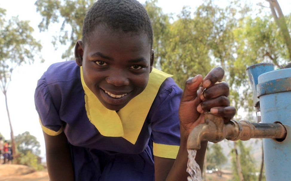 Living Schools Malawi: Eine Schülerin steht an einem Wasserhahn, aus dem sauberes Trinkwasser fließt