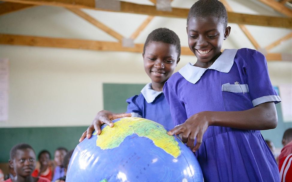 Living Schools Malawi: Zwei Schülerinnen stehen neben einem Globus.