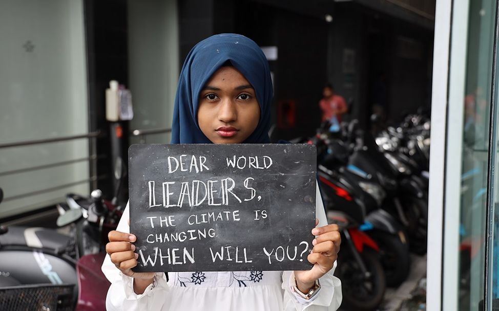 Malediven: Ein Mädchen hält eine Tafel vor ihren Körper Richtung Kamera.