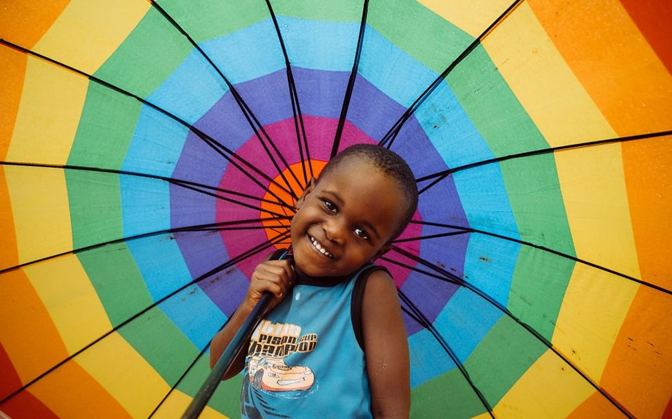 Mosambik: Ein Kind hält einen bunten Regenschirm in der Hand und lächelt.