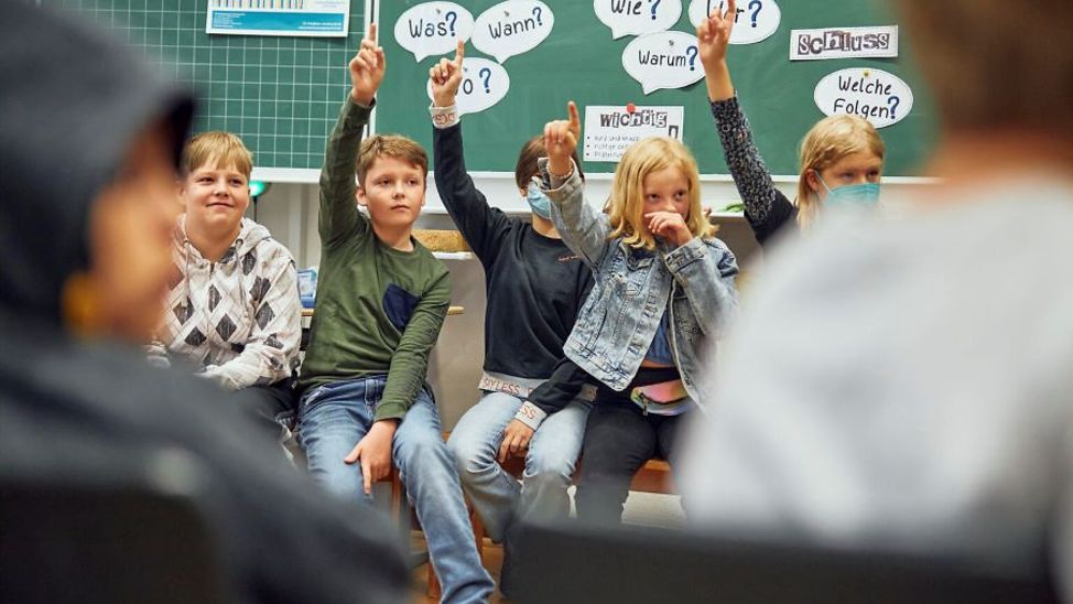 Deutschland: Schulkinder sitzen im Sitzkreis und melden sich.
