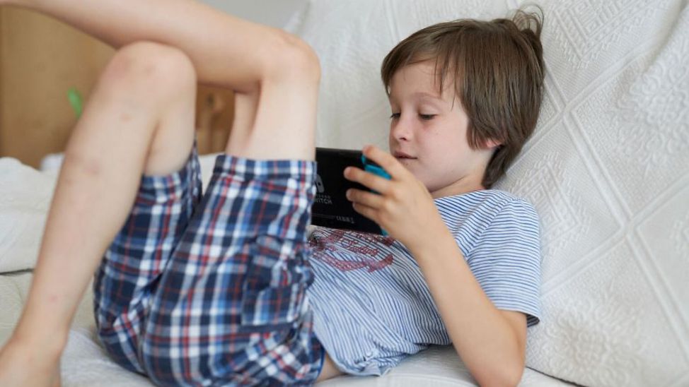 Deutschland: Ein Junge sitzt auf einer Couch und schaut auf ein Handy.