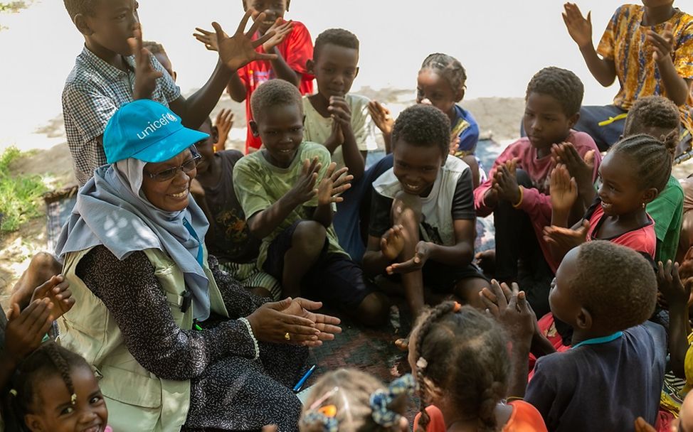 Sudan: Eine UNICEF-Mitarbeitende sitzt mit Kindern im Kreis und singt