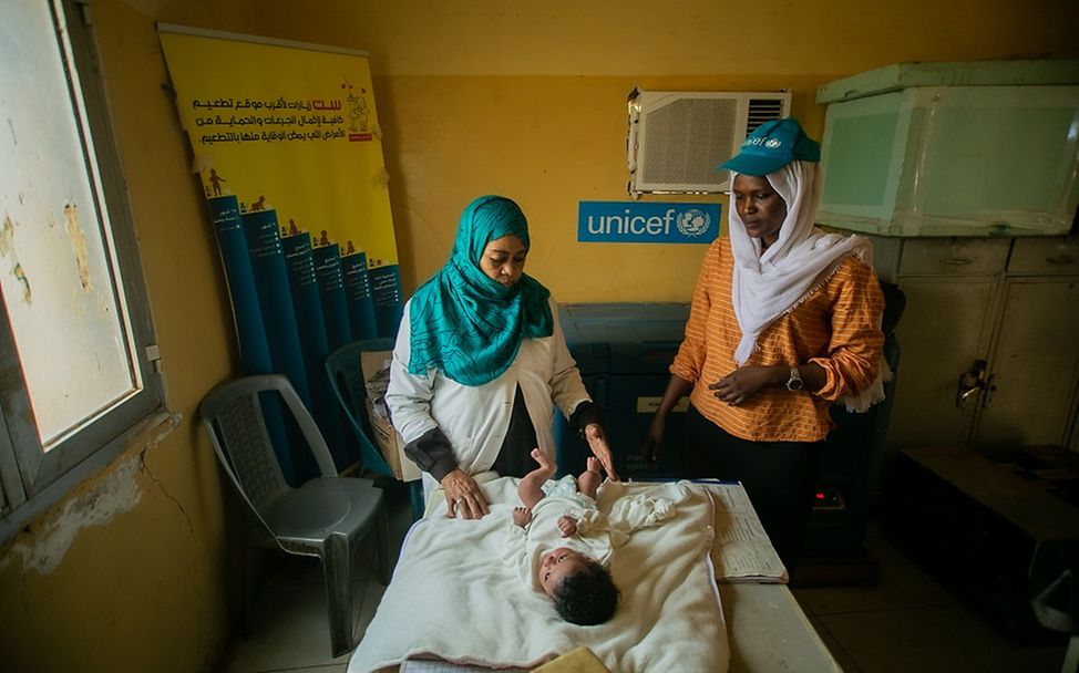 Sudan: Zwei Gesundheitshelferinnen stehen an einem Wickeltisch, auf dem ein Baby liegt.