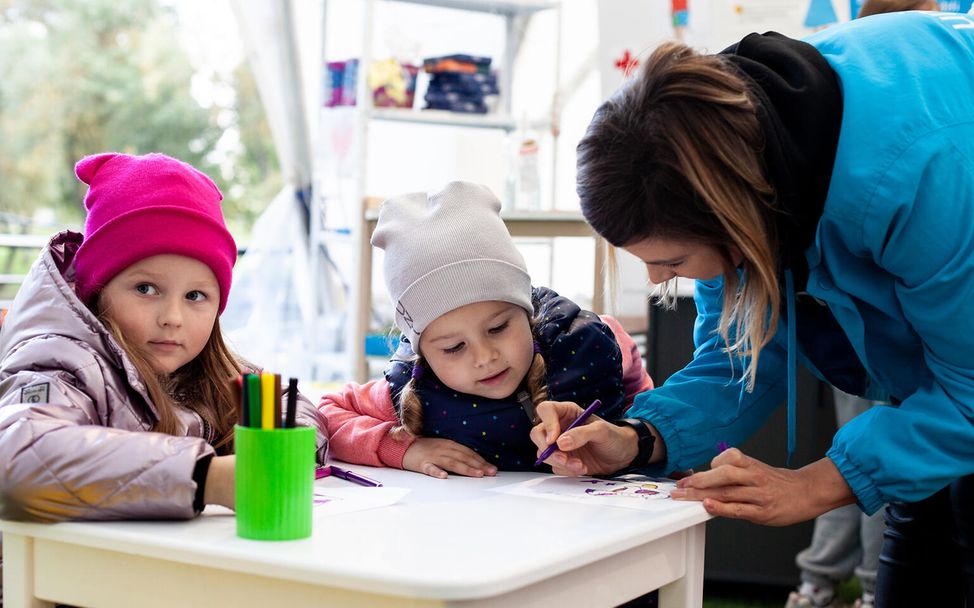 Spenden statt schenken Unternehmen: Eine Helferin malt mit zwei Kindern in einem Kinderzentrum in der Ukraine