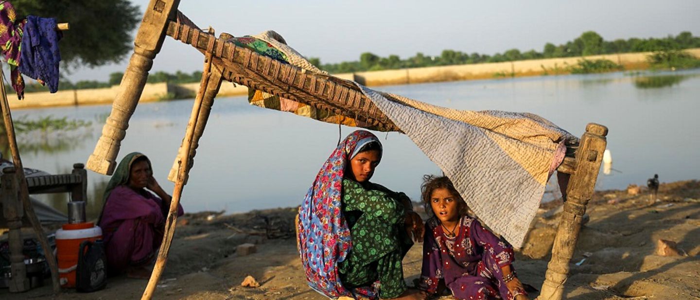 Flut Pakistan: Eine Mutter sitzt mit ihren Kindern unter einem behelfsmäßigen Zelt.