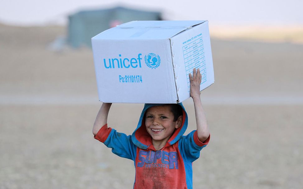 Originelle Geschenkideen für guten Zweck: Junge trägt einen Karton mit Hilfsgütern von UNICEF in Syrien