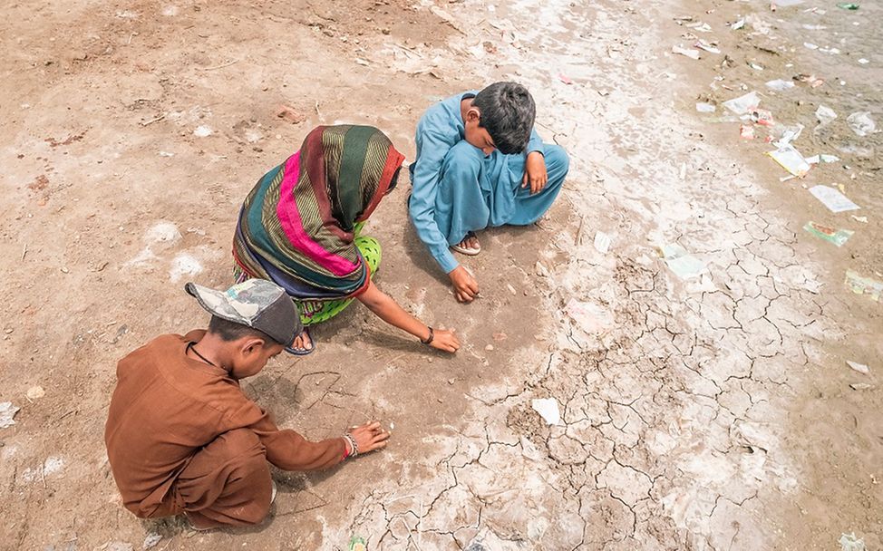 Drei Jungen spielen in einem ausgetrockneten Abschnitt eines einst überschwemmten Gebiets in Südpakistan.