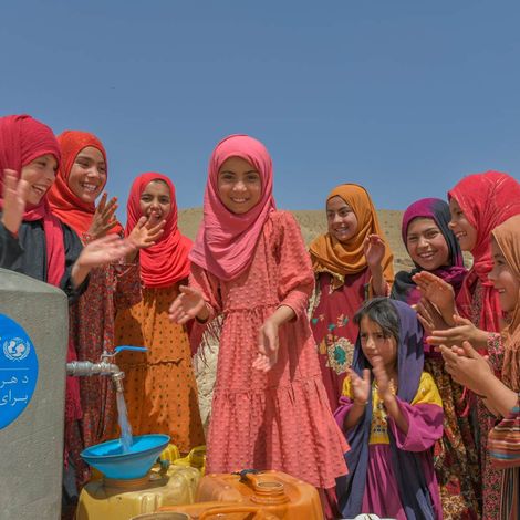 Mädchen in Afghanistan füllen an einem Brunnen Wasser in Kanister. 