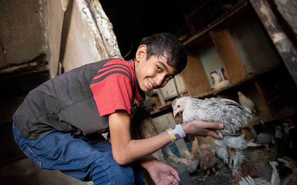 Ein Junge in Syrien spielt lächelnd mit einem Huhn. 