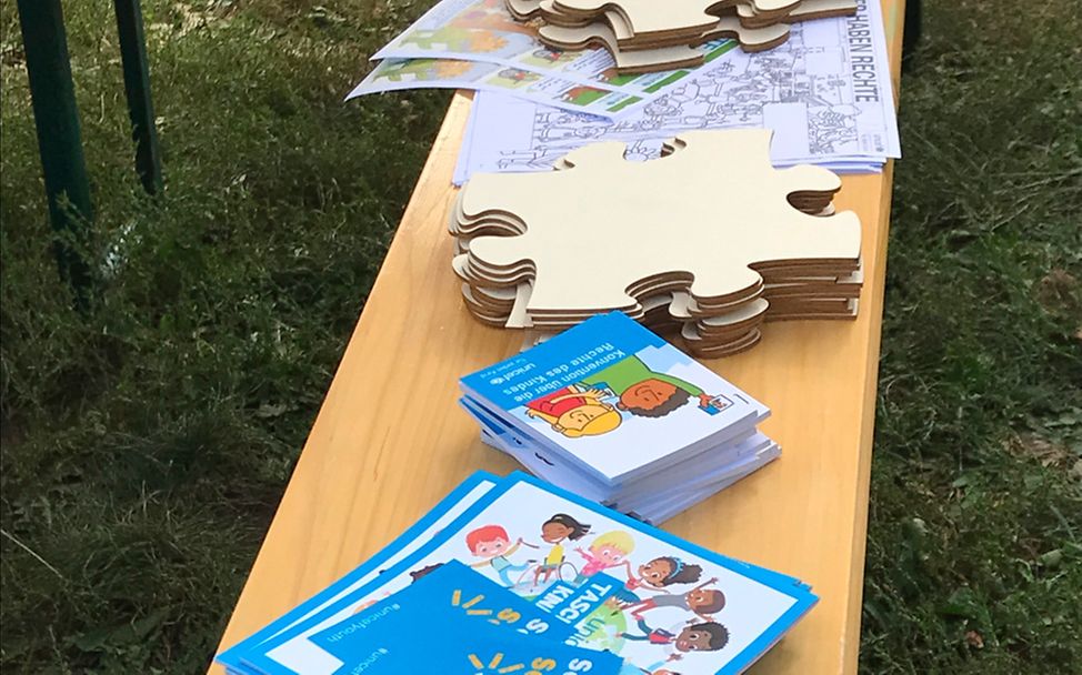Weltkindertag 2023 in Radebeul - Puzzleteile zum Bemalen und Kinderrechtebüchlein für Kinder liegen auf einer Bank