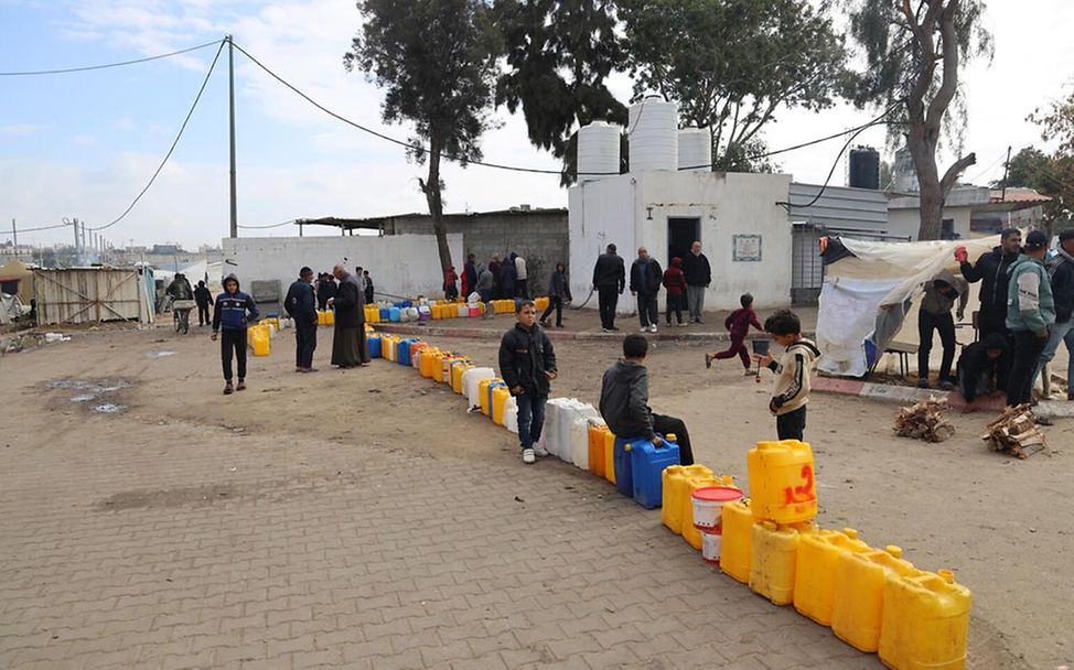 Kinder in Gaza: Wasserkanister stehen aufgereiht vor einer Ausgabe für Trinkwasser
