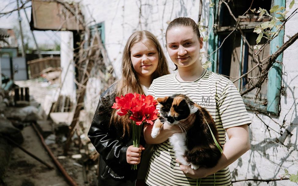 Ukraine Krieg Nothilfe: Zwei Mädchen stehen vor ihrem durch Raketen zerstörten Haus im Osten des Landes. 