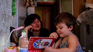 Jahrestag Ukraine-Krieg: Junge liest seiner Mutter am Küchentisch vor.