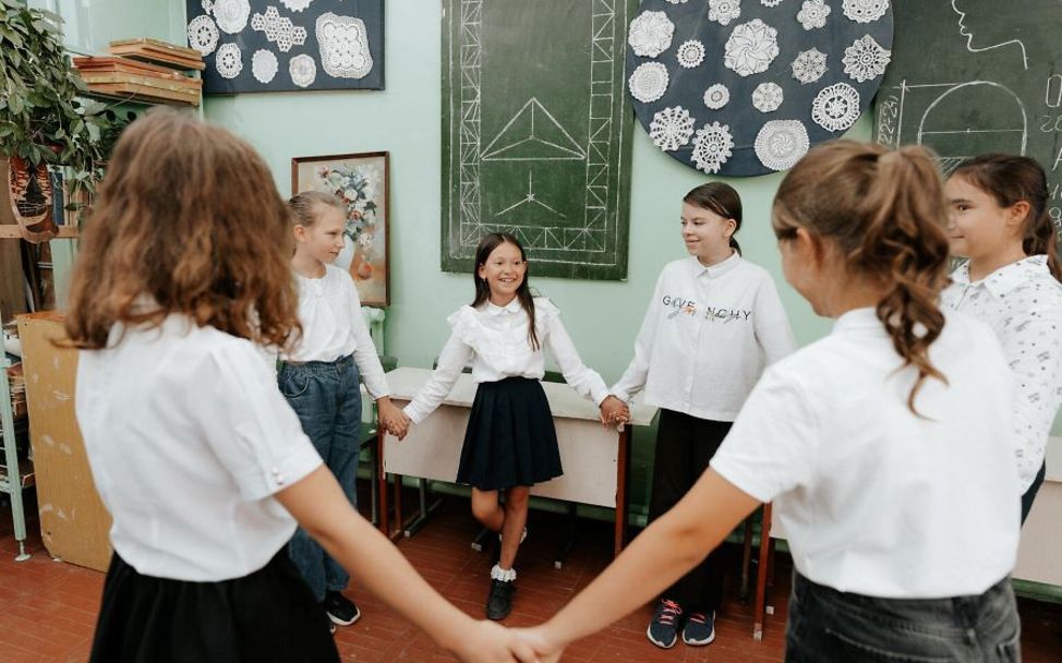 Jahrestag Ukraine-Krieg: Mädchen in Schuluniform stehen im Kreis und halten Hände. 