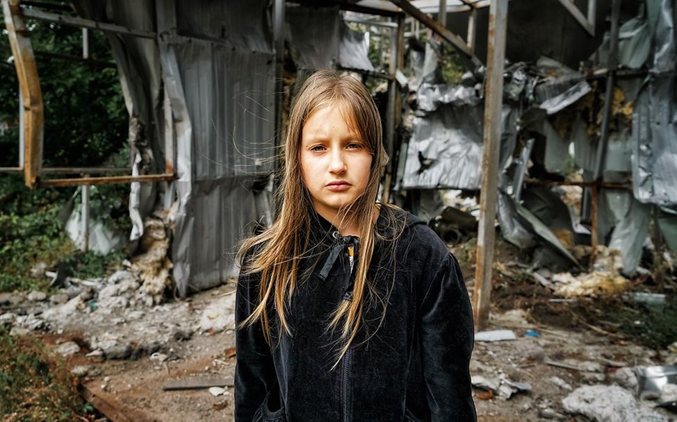 Ukraine: Die zehnjährige Arina steht vor einem zerstörten Gebäude in der Region Charkiw.