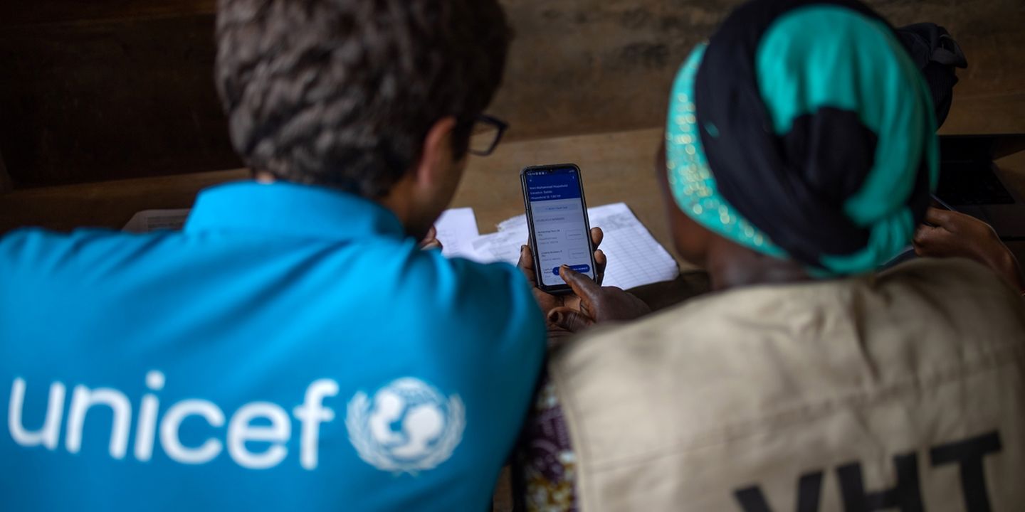 Blick über die Schulter eines UNICEF-Mitarbeiters und einer VHT-Mitarbeiterin auf ein Handy. 
