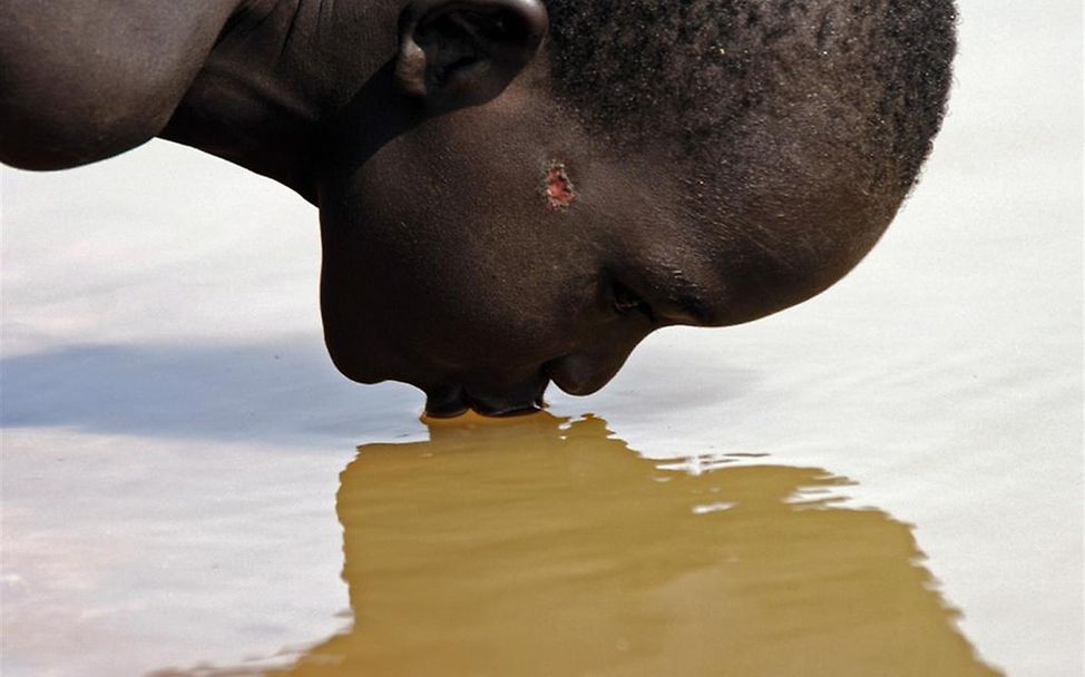 Junge trinkt aus dem Fluss am Rande des Dorfes. © UNICEF/Cranston