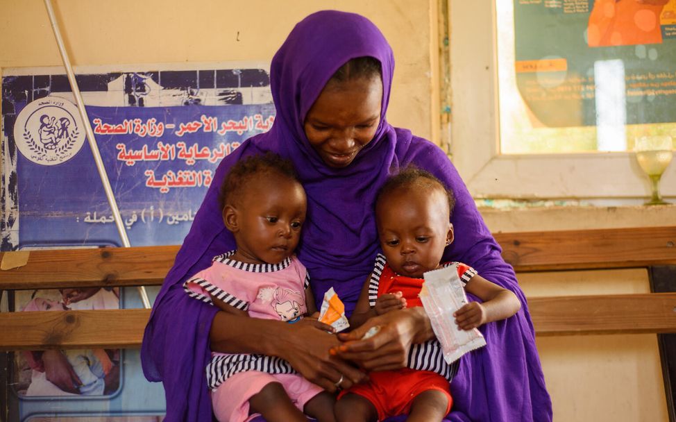 Sudan: Mutter hält ihre mangelernährten Töchter im Arm 