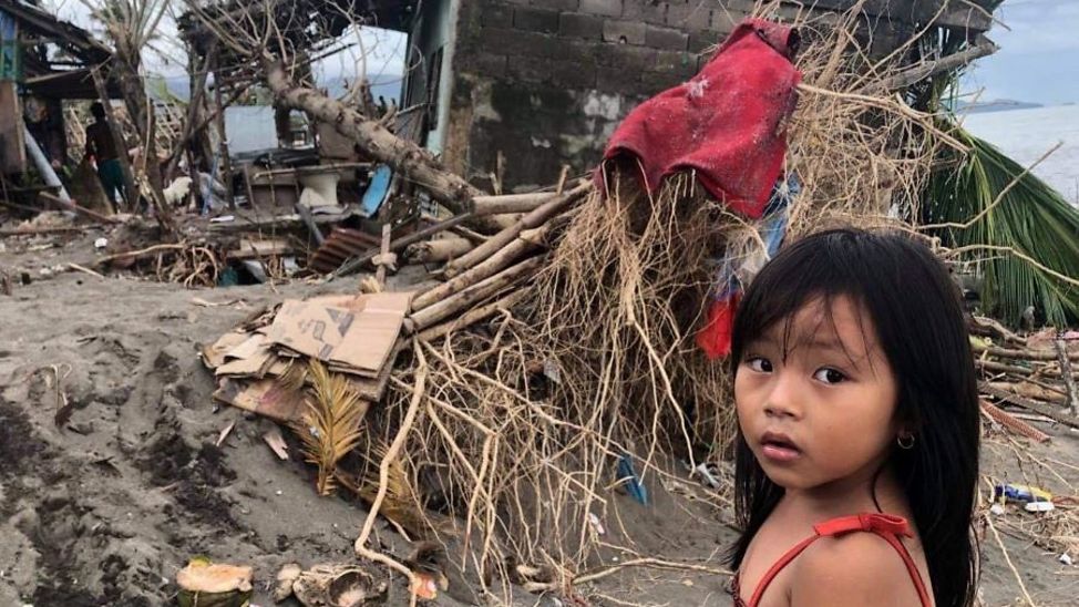 Mädchen steht vor durch Taifun zerstörte Häuser.
