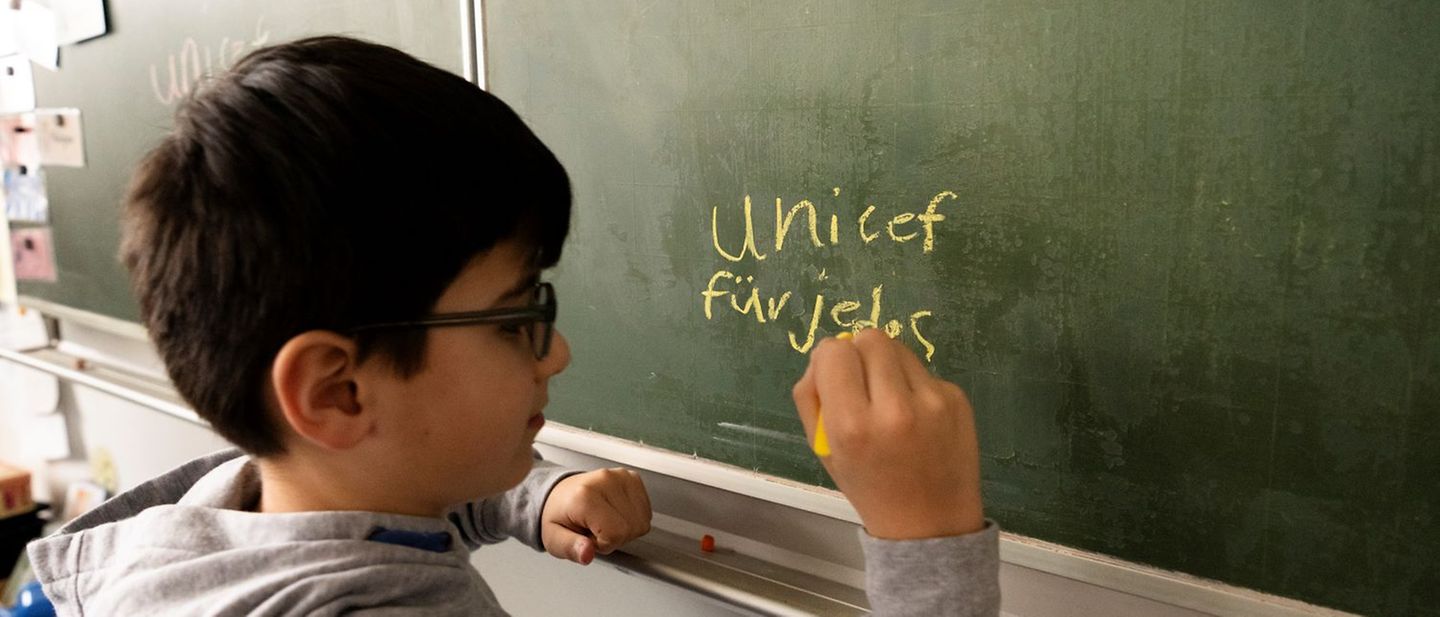 Ein Junge schreibt an die Tafel. Seine Klasse nimmt an der UNICEF-Spendenaktion "Lesen für UNICEF" teil.