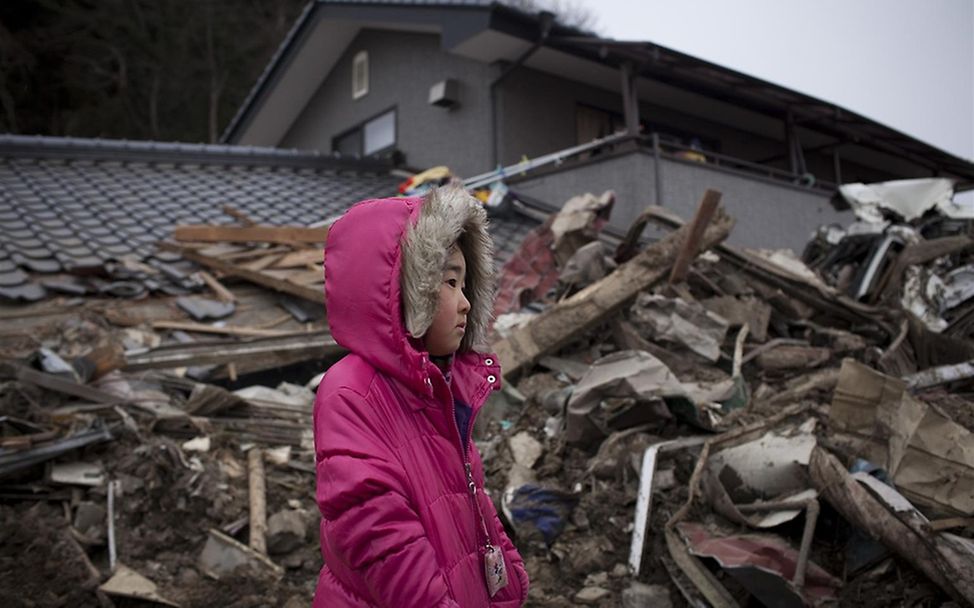 Ein Mädchen steht vor den Trümmern ihres zu Hauses, das durch den Tsunami zerstört wurde.© UNICEF/Dean