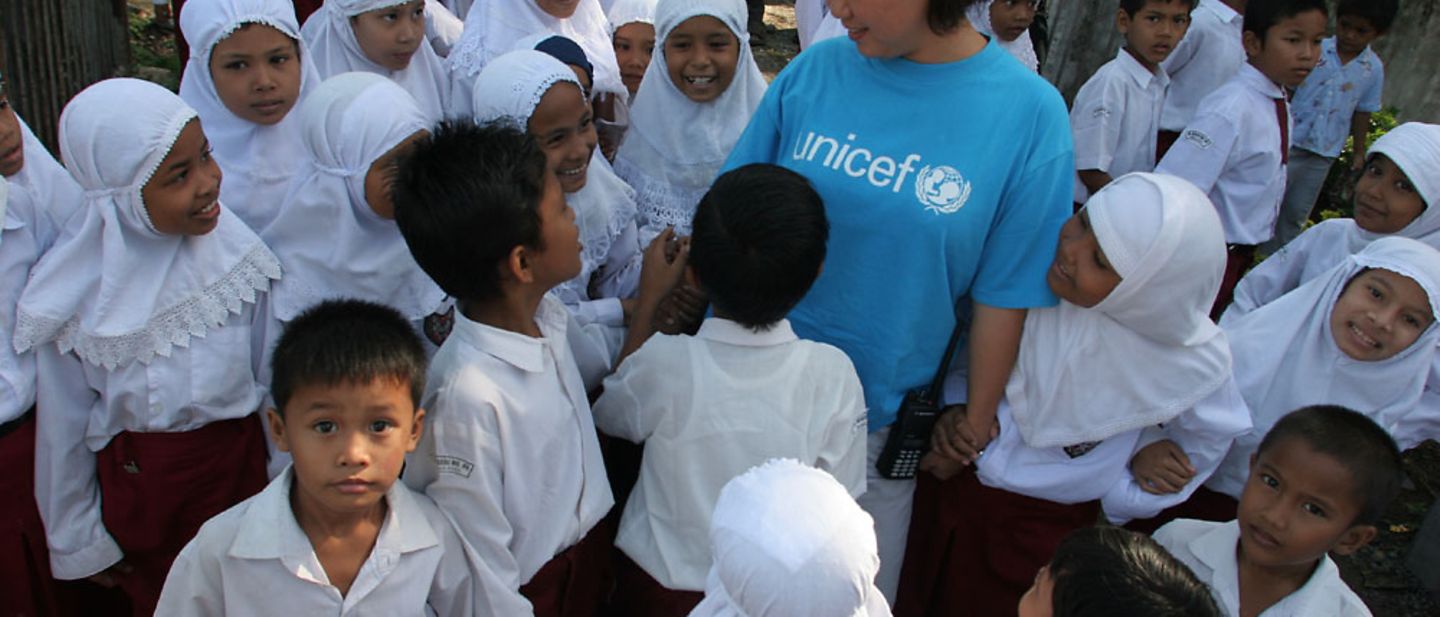 Indonesien: UNICEF-Mitarbeiterin steht gemeinsam mit Schülern vor einer Schule.